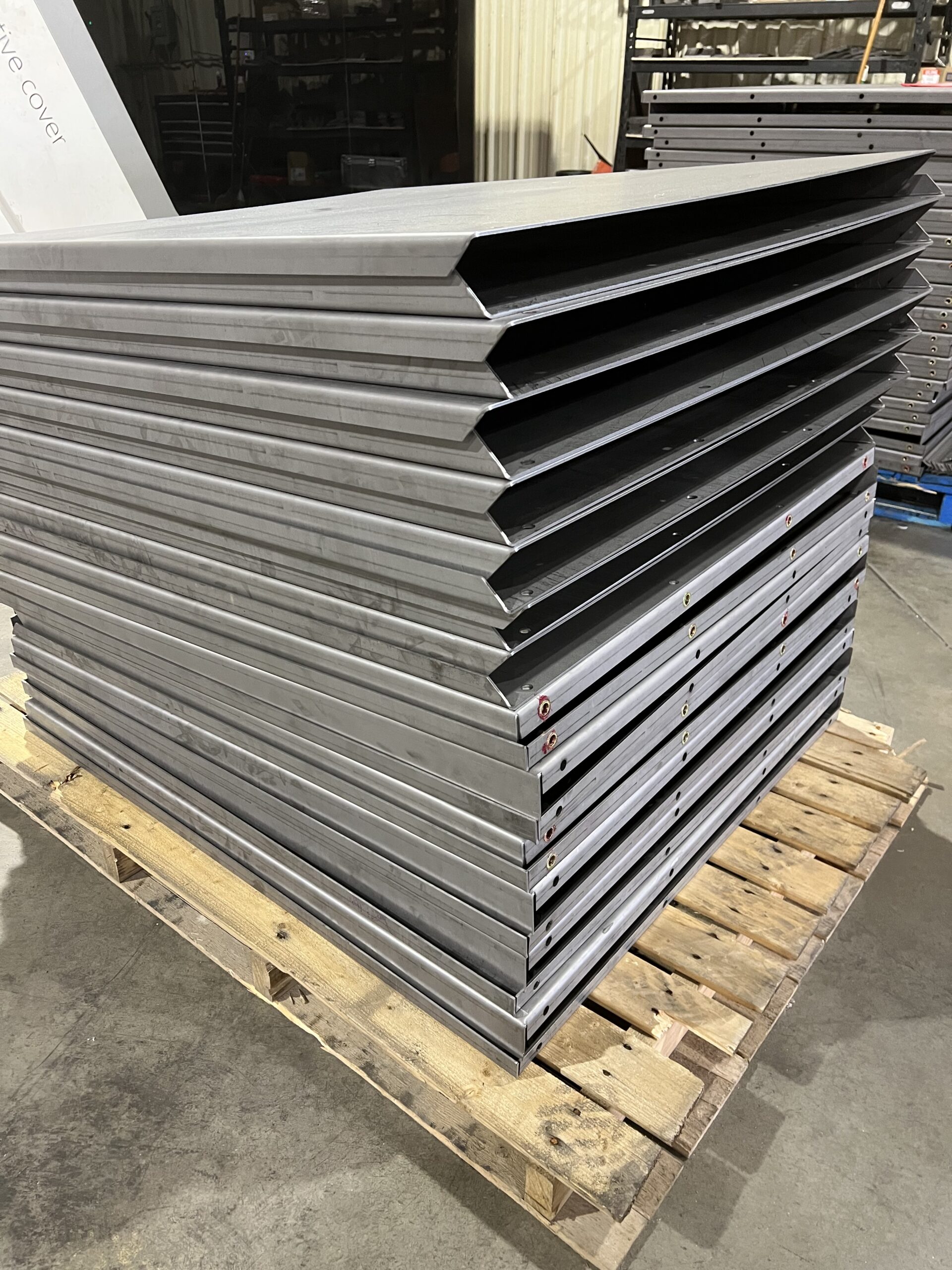 A stack of neatly fabricated metal panels with uniform edges, arranged on a wooden pallet in a workshop, showcasing precision and durability in manufacturing.